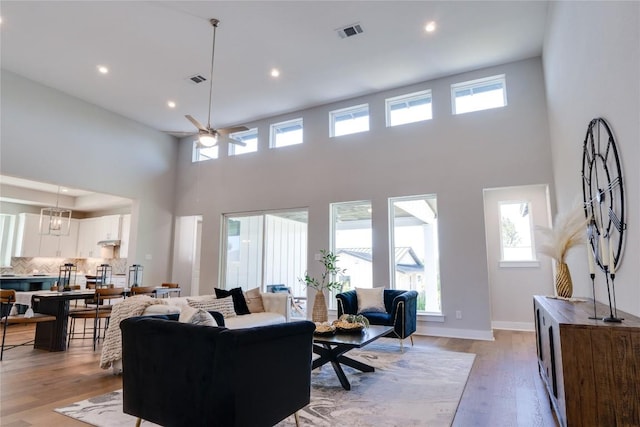 living room with ceiling fan, a high ceiling, and light hardwood / wood-style flooring