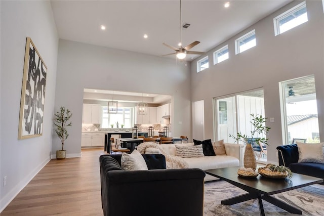 living room with ceiling fan, light hardwood / wood-style flooring, and a high ceiling