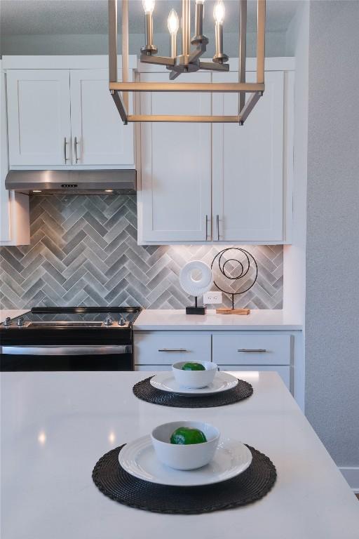 kitchen with tasteful backsplash, electric stove, white cabinets, and decorative light fixtures