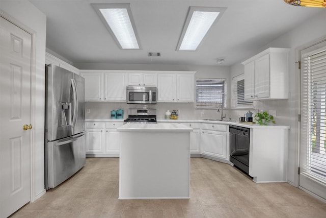 kitchen featuring appliances with stainless steel finishes, sink, light tile patterned floors, white cabinets, and a kitchen island