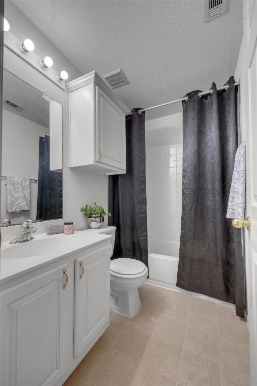 full bathroom featuring shower / bathtub combination with curtain, tile patterned flooring, a textured ceiling, toilet, and vanity