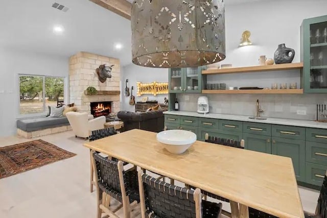 kitchen featuring tasteful backsplash, a stone fireplace, and green cabinetry