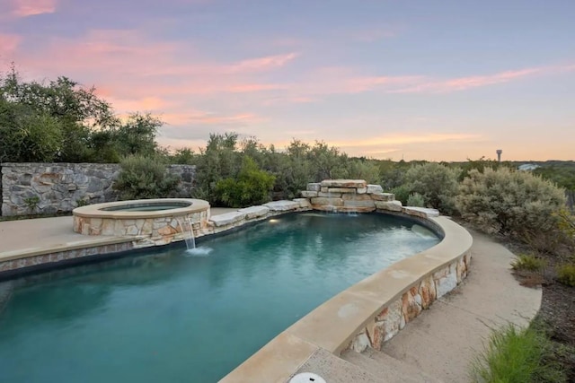 pool at dusk with pool water feature and an in ground hot tub