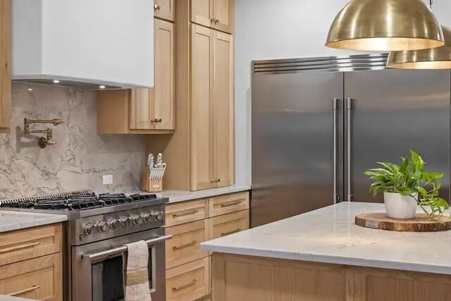 kitchen with light brown cabinetry, high quality appliances, tasteful backsplash, light stone countertops, and wall chimney range hood