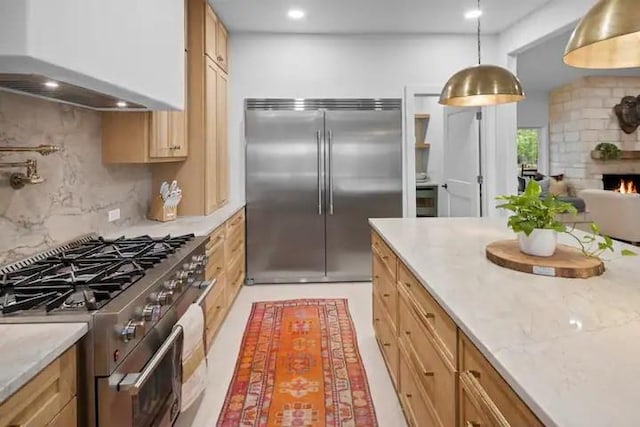 kitchen with pendant lighting, a fireplace, high quality appliances, decorative backsplash, and wall chimney range hood