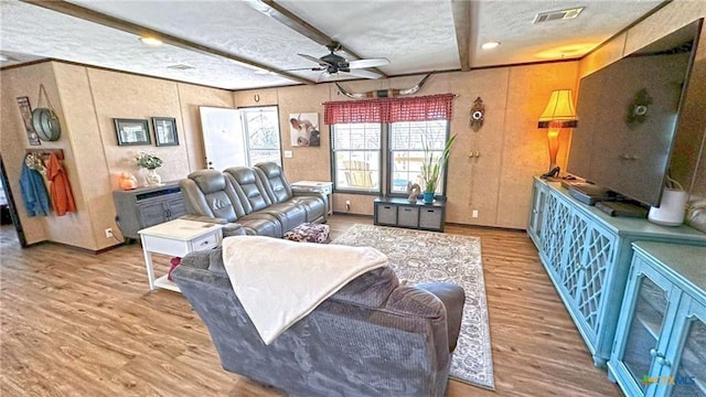 living room with ceiling fan, beam ceiling, light hardwood / wood-style flooring, and a textured ceiling