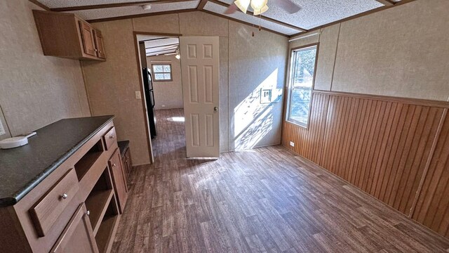 interior space with ceiling fan, vaulted ceiling, wood-type flooring, and wood walls