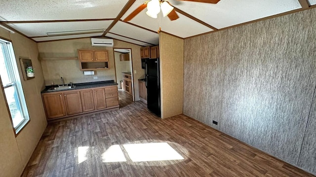 kitchen featuring sink, black fridge, vaulted ceiling, a wall unit AC, and hardwood / wood-style flooring