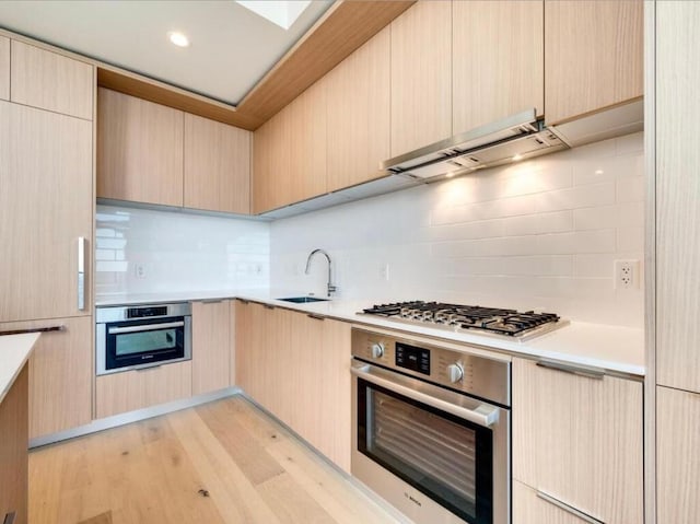 44 E Ave Unit 2808, Austin, TX 78701 - kitchen with stainless steel appliances, under cabinet range hood, light brown cabinets, decorative backsplash, and light wood-style floors