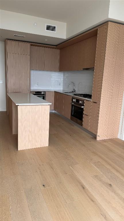 kitchen featuring sink, a center island, stainless steel appliances, light hardwood / wood-style floors, and decorative backsplash