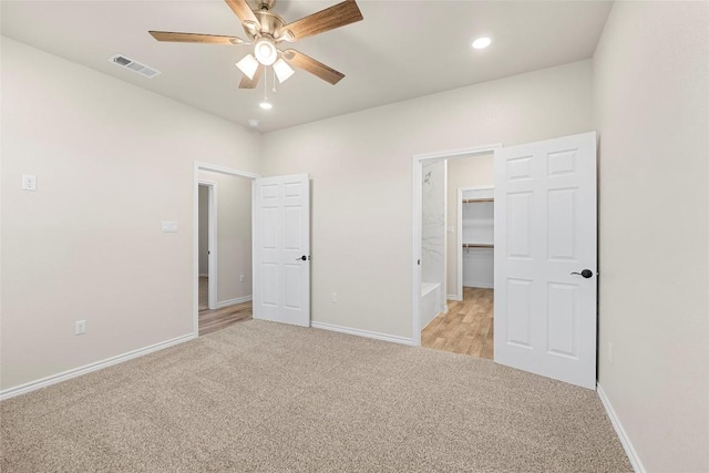 unfurnished bedroom featuring ceiling fan, a spacious closet, light carpet, and a closet