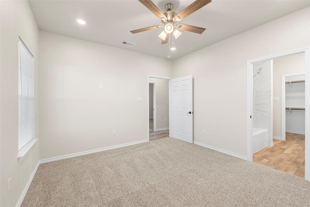 unfurnished bedroom with ensuite bath, a spacious closet, ceiling fan, light colored carpet, and a closet