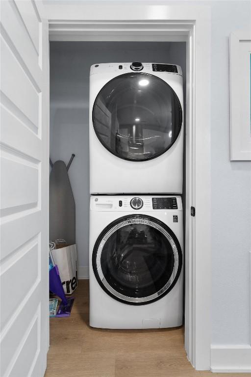 clothes washing area with stacked washer / drying machine and light wood-type flooring