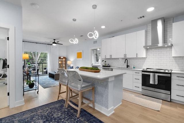 kitchen with wall chimney exhaust hood, stainless steel electric stove, sink, white cabinets, and a center island