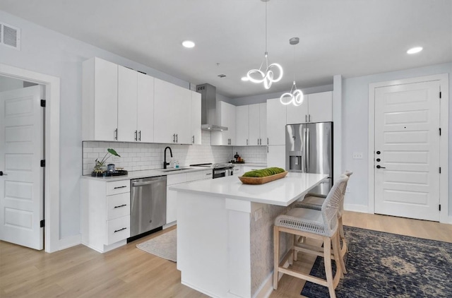 kitchen featuring stainless steel appliances, wall chimney range hood, white cabinets, a center island, and light hardwood / wood-style floors