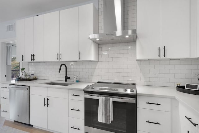 kitchen with sink, wall chimney exhaust hood, tasteful backsplash, white cabinetry, and stainless steel appliances