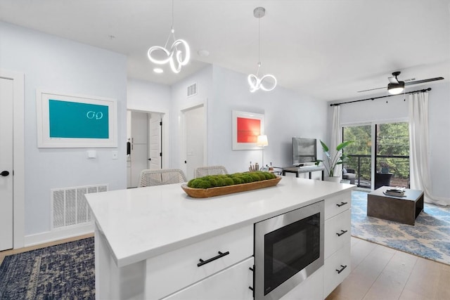 kitchen with built in microwave, decorative light fixtures, a center island, light hardwood / wood-style floors, and white cabinetry