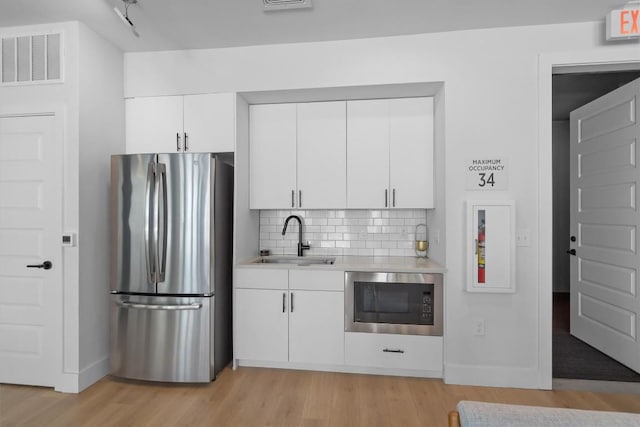 kitchen with stainless steel refrigerator, built in microwave, tasteful backsplash, sink, and white cabinets