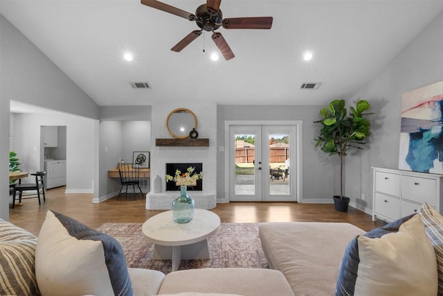 living room with french doors, light wood-type flooring, a brick fireplace, ceiling fan, and washer / dryer