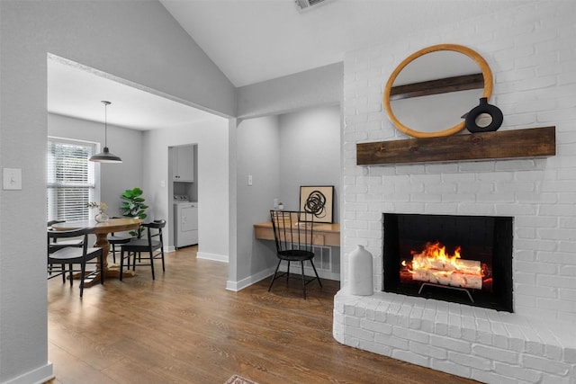 living room featuring hardwood / wood-style flooring, washer / dryer, a fireplace, and vaulted ceiling