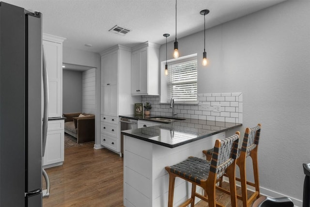 kitchen featuring white cabinetry, sink, stainless steel appliances, decorative light fixtures, and a kitchen bar