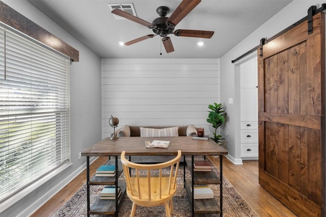 office area featuring ceiling fan, a barn door, light hardwood / wood-style floors, and a textured ceiling