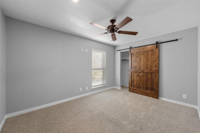 unfurnished bedroom featuring carpet flooring, a textured ceiling, ceiling fan, a barn door, and a closet