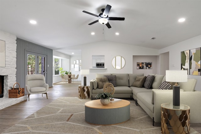 living room with a stone fireplace, ceiling fan, wood-type flooring, and lofted ceiling