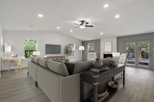 living room featuring a wealth of natural light, ceiling fan, light hardwood / wood-style floors, a stone fireplace, and lofted ceiling