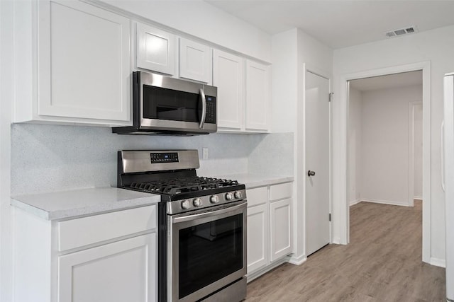 kitchen with white cabinets, light hardwood / wood-style flooring, appliances with stainless steel finishes, and tasteful backsplash