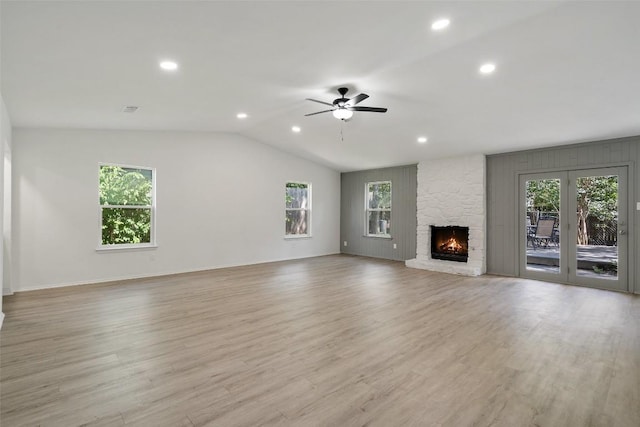 unfurnished living room with ceiling fan, light hardwood / wood-style floors, a stone fireplace, and vaulted ceiling