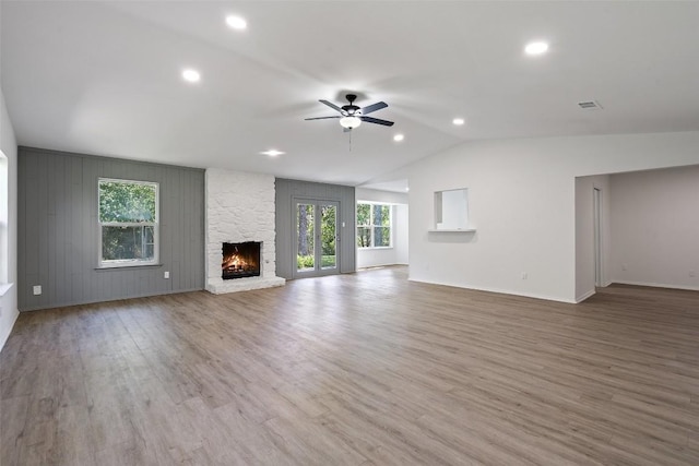 unfurnished living room featuring hardwood / wood-style flooring, ceiling fan, a stone fireplace, and vaulted ceiling