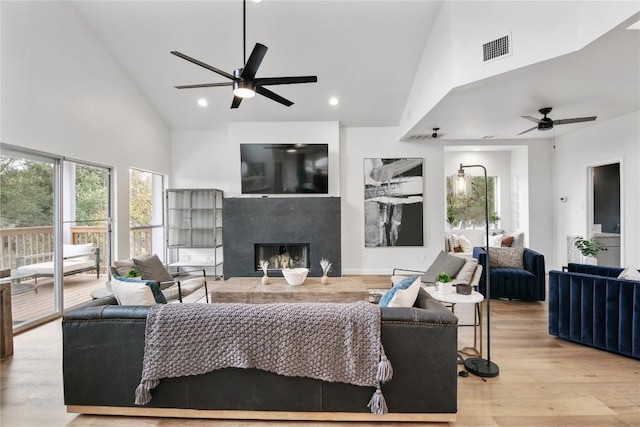 living room featuring a premium fireplace, high vaulted ceiling, light hardwood / wood-style floors, and ceiling fan