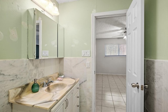 bathroom with ceiling fan, tile patterned flooring, a textured ceiling, vanity, and tile walls