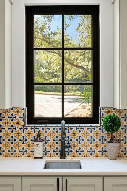 interior details featuring decorative backsplash, white cabinetry, and sink