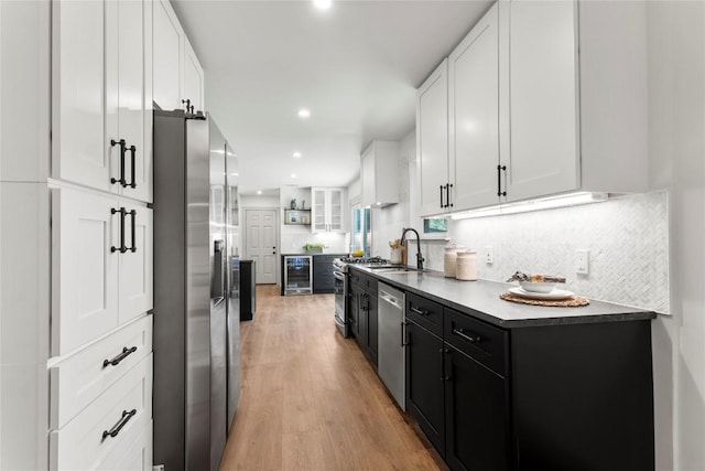 kitchen featuring sink, beverage cooler, appliances with stainless steel finishes, white cabinets, and light wood-type flooring