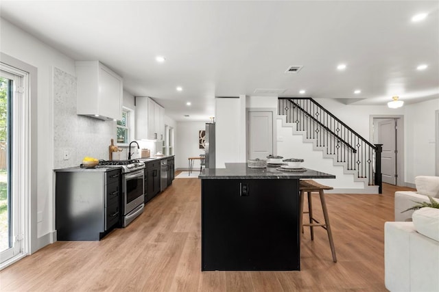 kitchen featuring a center island, dark stone countertops, light wood-type flooring, gas stove, and white cabinetry