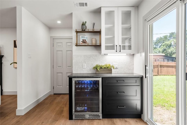 bar featuring tasteful backsplash, white cabinets, beverage cooler, and light hardwood / wood-style floors