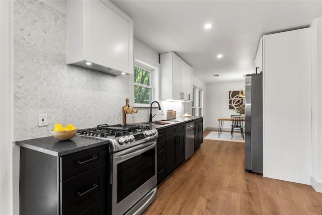 kitchen featuring white cabinetry, sink, stainless steel appliances, backsplash, and light wood-type flooring