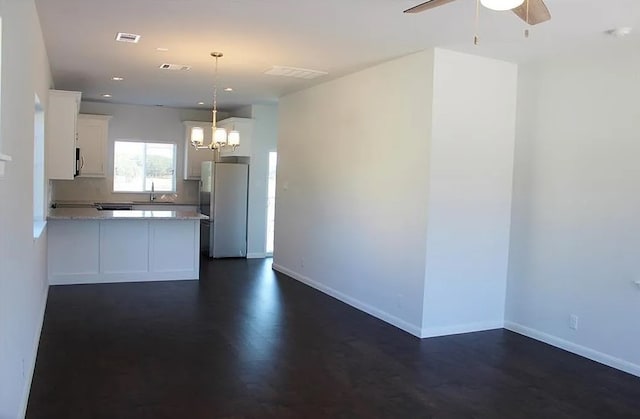 kitchen with pendant lighting, white cabinets, ceiling fan with notable chandelier, white fridge, and light stone counters