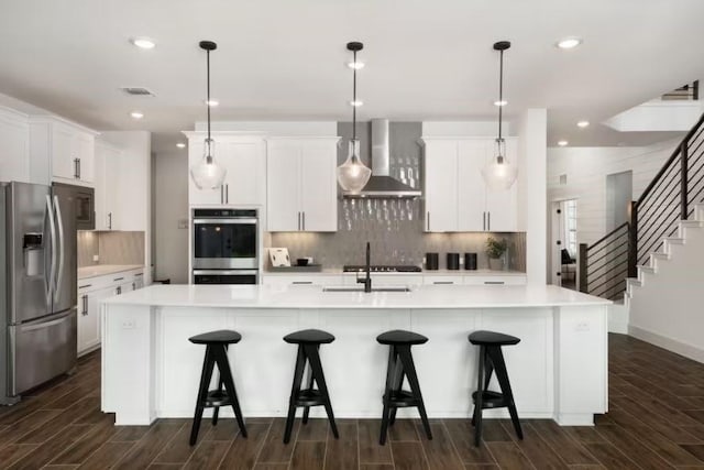 kitchen featuring stainless steel appliances, hanging light fixtures, wall chimney exhaust hood, and an island with sink