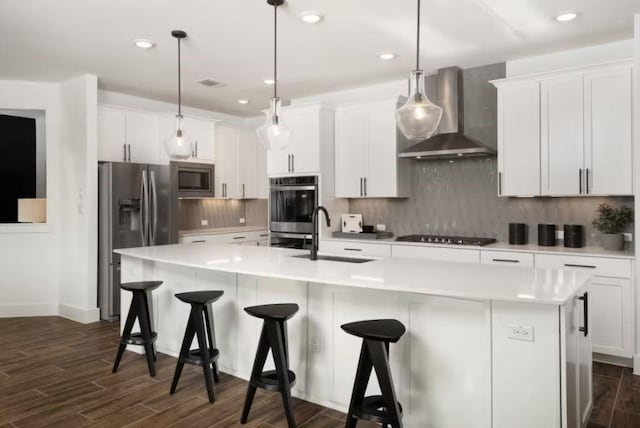 kitchen featuring wall chimney range hood, stainless steel appliances, and a kitchen island with sink