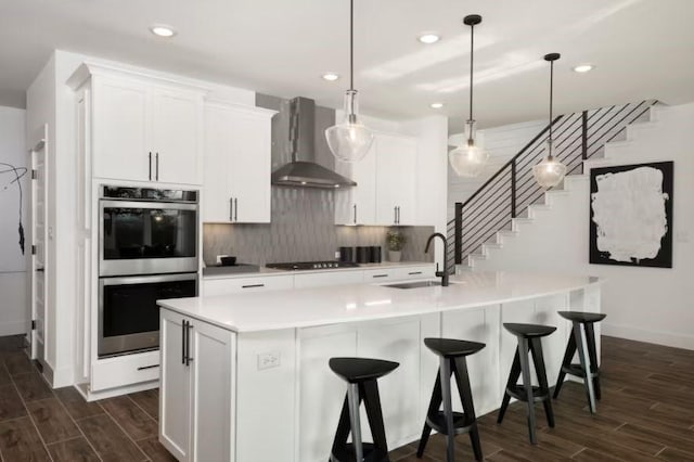 kitchen with white cabinetry, sink, wall chimney exhaust hood, double oven, and decorative light fixtures