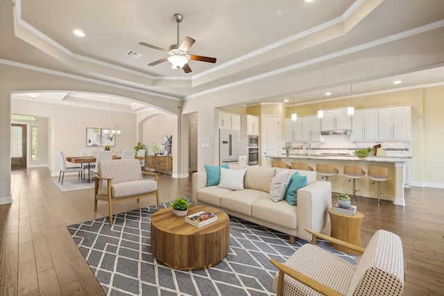 living room with a raised ceiling, dark hardwood / wood-style flooring, and ceiling fan with notable chandelier