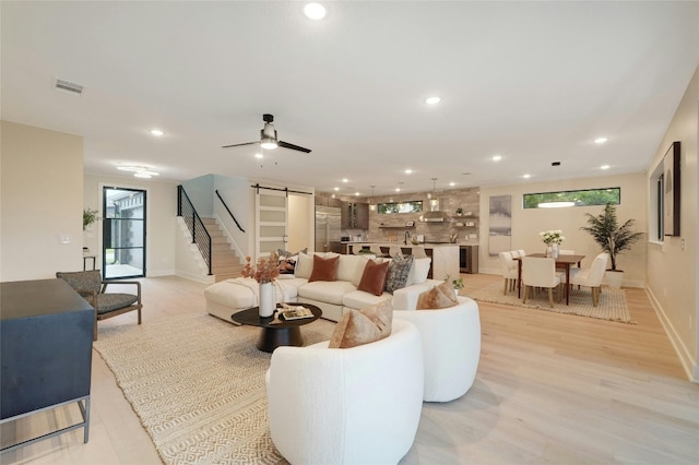 living room with a barn door, ceiling fan, and light hardwood / wood-style flooring