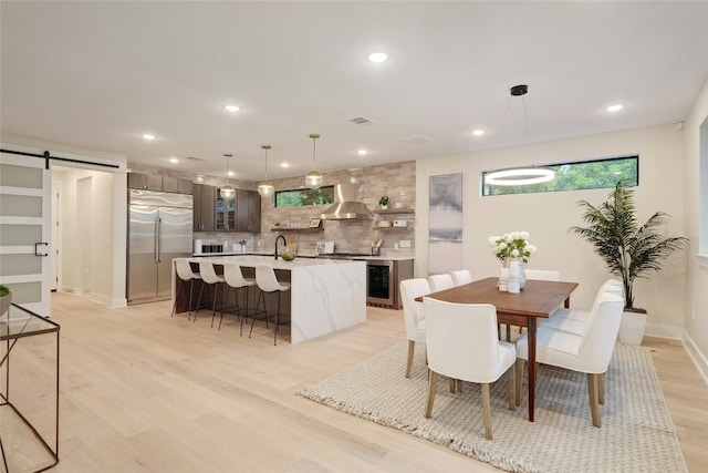 dining area with a barn door, light wood-type flooring, and beverage cooler