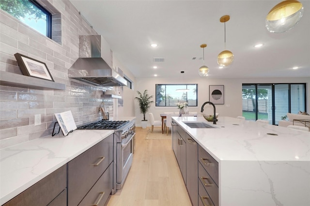 kitchen featuring sink, wall chimney range hood, high end stainless steel range oven, backsplash, and pendant lighting