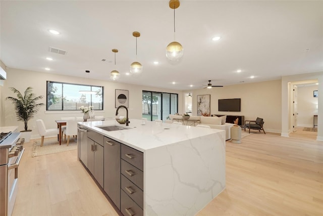 kitchen with light stone counters, ceiling fan, sink, light hardwood / wood-style flooring, and hanging light fixtures