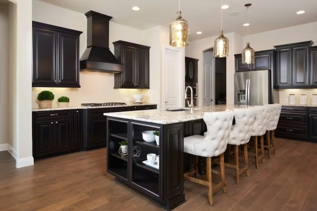 kitchen with premium range hood, a kitchen island with sink, dark wood-type flooring, and appliances with stainless steel finishes