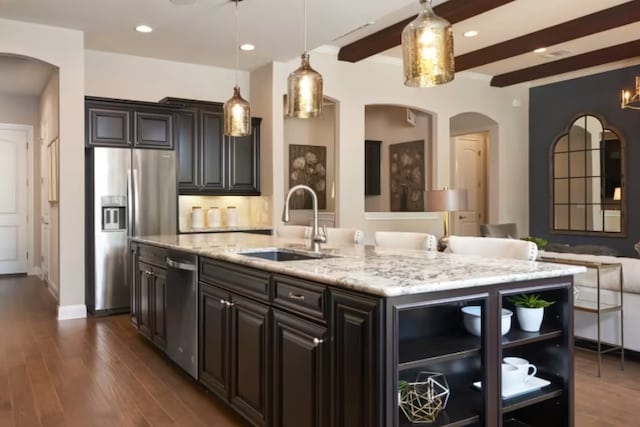 kitchen with a kitchen island with sink, sink, appliances with stainless steel finishes, decorative light fixtures, and beam ceiling